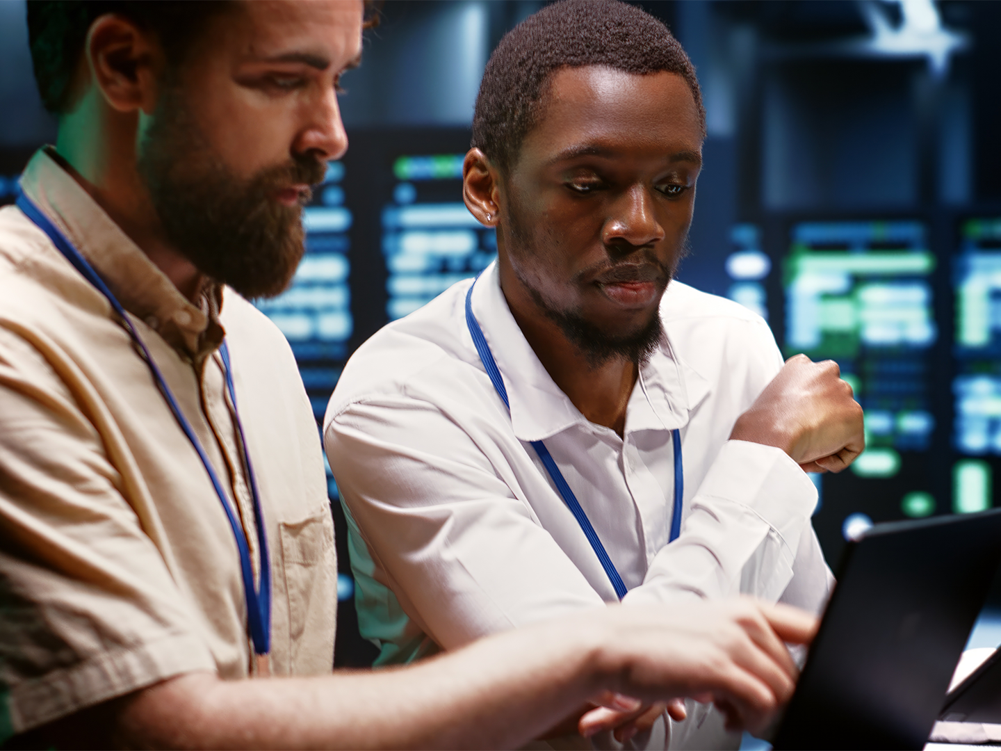 Two data center engineers review information on a tablet with server racks in the background.