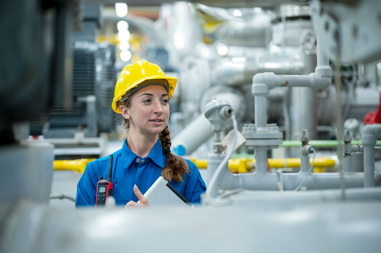 Woman in a hard hat checking equipment in a factory.