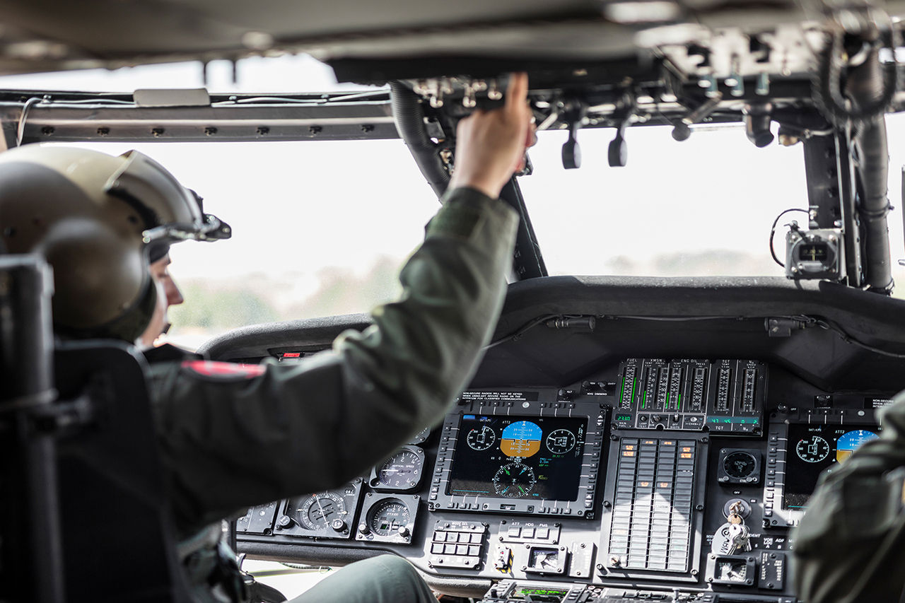  A pilot operates a military helicopter cockpit filled with digital displays and controls.  