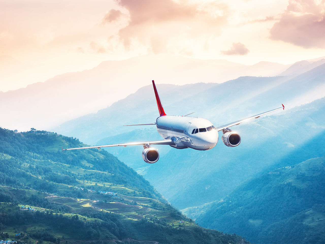 Commercial aircraft flying over a mountainous landscape at sunrise. 