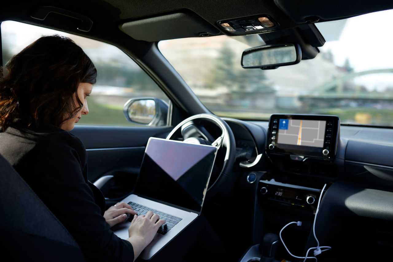 A woman using a laptop in an automobile.