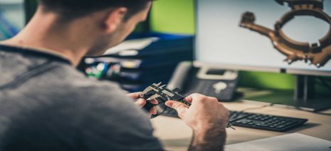 デスクトップコンピューターでの作業中に、キャリパーを使用してパーツの寸法をチェックするエンジニア。